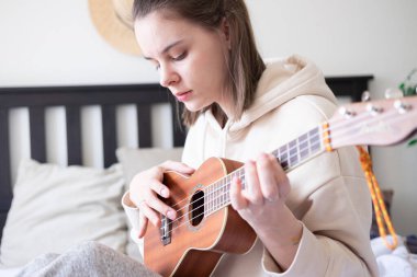 Evde gitar çalan genç bir kadının portresini yakından çek. Evde kendini karantinaya alarak zaman geçirmek.