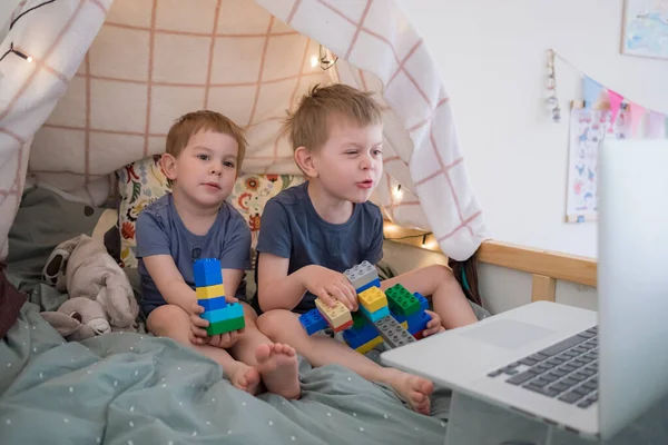 Chłopcy siedzą na łóżku z laptopem. Oglądanie kreskówek, wideo czat, edukacja na odległość. Zamknięcie, kwarantanna. Rodzina stylu życia — Zdjęcie stockowe