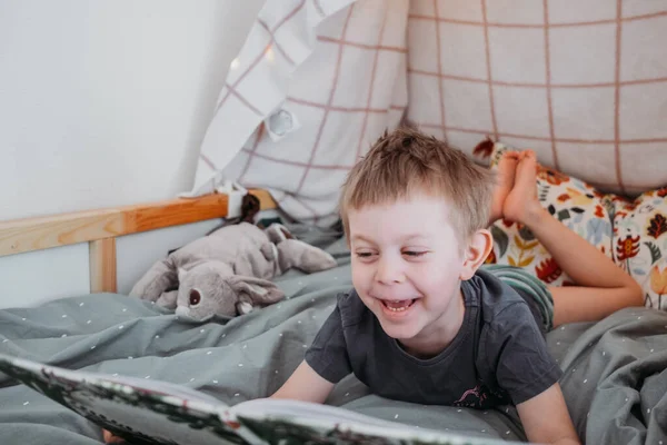 Enfant d'âge préscolaire lisant un livre allongé dans son lit. passer du temps à la maison. Concept de famille Lifestyle — Photo