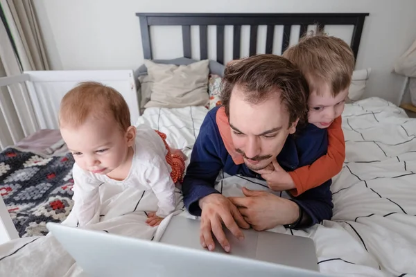 Man probeert thuis via laptop te werken tijdens quarantaine met peuter die op bed springt. Het gezinsleven tijdens de isolatie. Blijf thuis. Thuis werken, thuiskantoor — Stockfoto