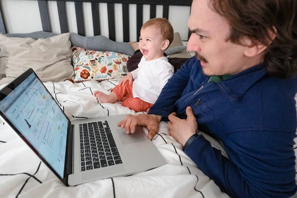 Mężczyzna próbujący pracować przez laptopa w domu podczas kwarantanny z niemowlęciem. Życie rodzinne podczas samoizolacji. Zostań w domu. Praca w domu, domowe biuro — Zdjęcie stockowe