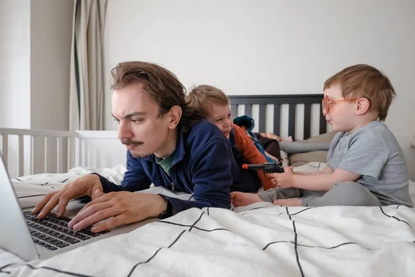 Życie rodzinne podczas samoizolacji. Zostań w domu. Człowiek próbujący pracować przez laptopa w domu podczas kwarantanny z dziećmi bawiącymi się w okolicy. Praca w domu, domowe biuro — Zdjęcie stockowe