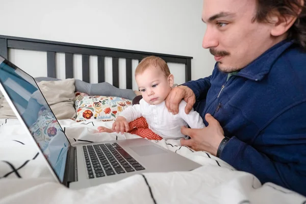 Mężczyzna próbujący pracować przez laptopa w domu podczas kwarantanny z niemowlęciem. Życie rodzinne podczas samoizolacji. Zostań w domu. Praca w domu, domowe biuro — Zdjęcie stockowe