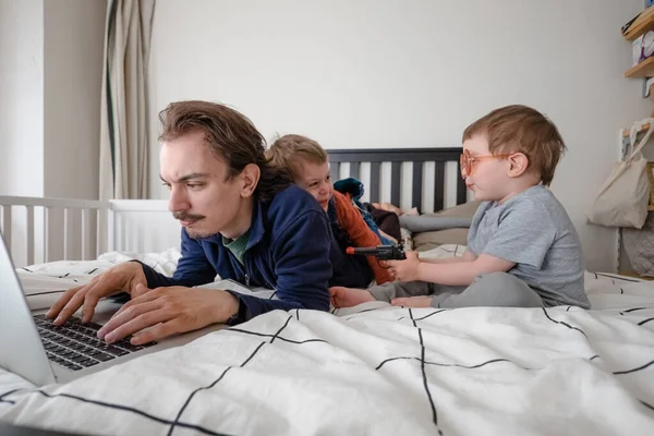 Życie rodzinne podczas samoizolacji. Zostań w domu. Człowiek próbujący pracować przez laptopa w domu podczas kwarantanny z dziećmi bawiącymi się w okolicy. Praca w domu, domowe biuro — Zdjęcie stockowe