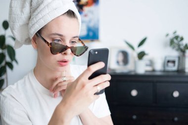 Kafasında havlu olan, güneş gözlüklü, sohbet eden ve cep telefonuyla fotoğraf çeken güzel bir kadın resmi. Sabah rutini konsepti. 