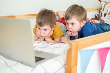 Evde yatakta uzanmış laptopa bakan iki çocuk görüntülü konuşma yapıyor, uzaktan eğitim alıyor, yeni şeyler öğreniyor, çizgi film seyrediyor.. 