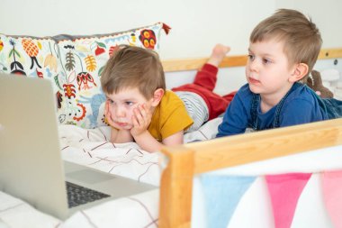 Evde yatakta uzanmış laptopa bakan iki çocuk görüntülü konuşma yapıyor, uzaktan eğitim alıyor, yeni şeyler öğreniyor, çizgi film seyrediyor.. 