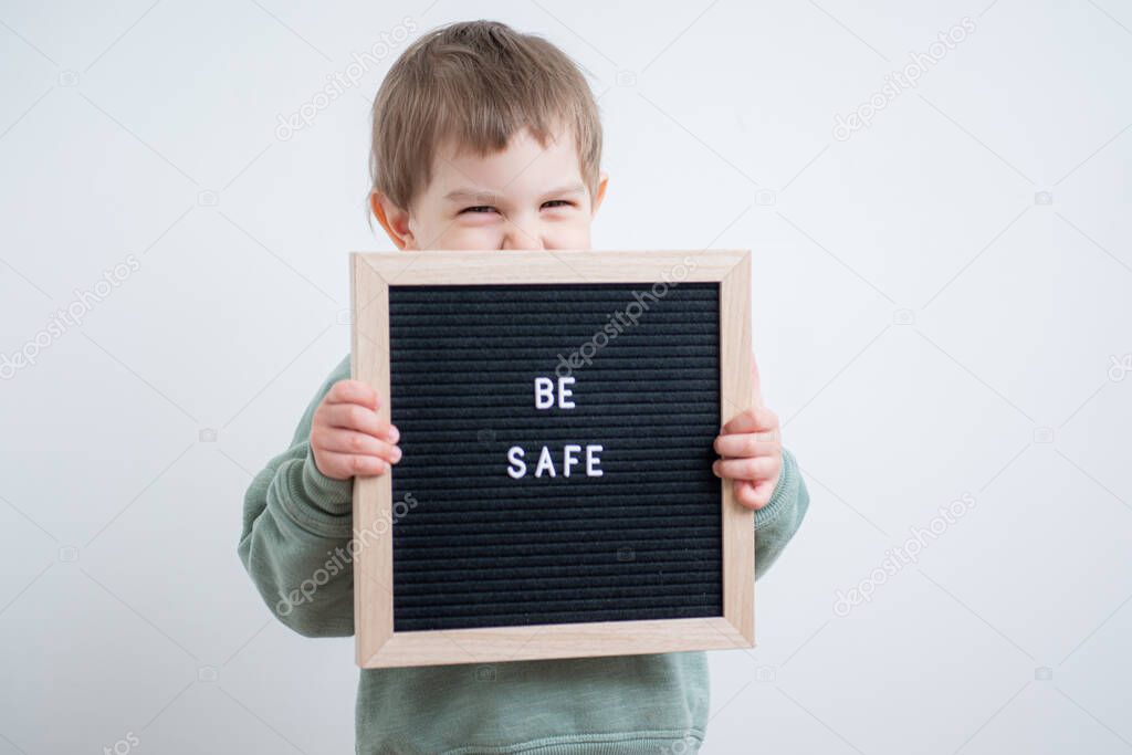 Toddler boy holding a felt letter-boad written Be safe. Stay home because of quarantine and self isolation. Social distancing. Minimalism concept