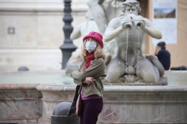 Roma, İtalya 9 Mayıs 2020: Pembe şapkalı ve maskeli kadın, Roma 'daki Piazza Navona' daki Bernini çeşmesine bakıyor. Covid-19 acil karantinasından sonra İtalya 'da ikinci aşamaya başlayan ilk hafta sonu..