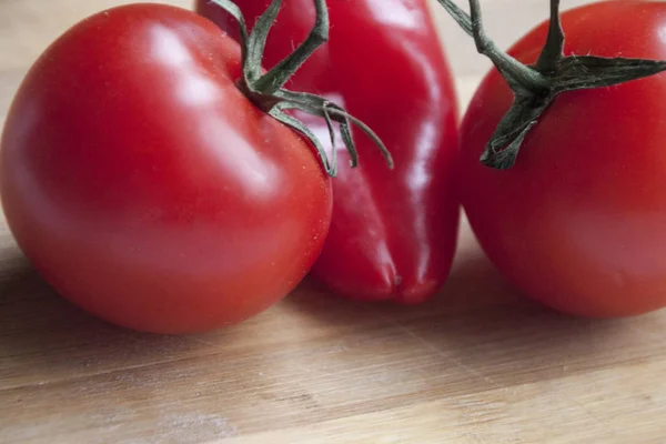 Rode peper tussen twee tomaten op houten bureau — Stockfoto