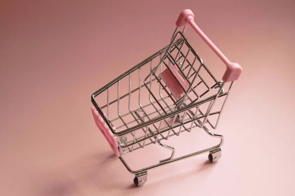 购物车。空超市手推车上粉红色的背景。消费主义概念照片. — 图库照片