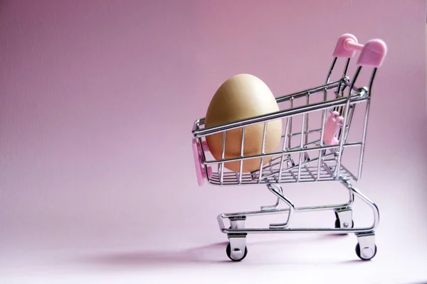 购物车 超市手推车上满是粉红色背景的大鸡蛋 消费主义概念照片 — 图库照片