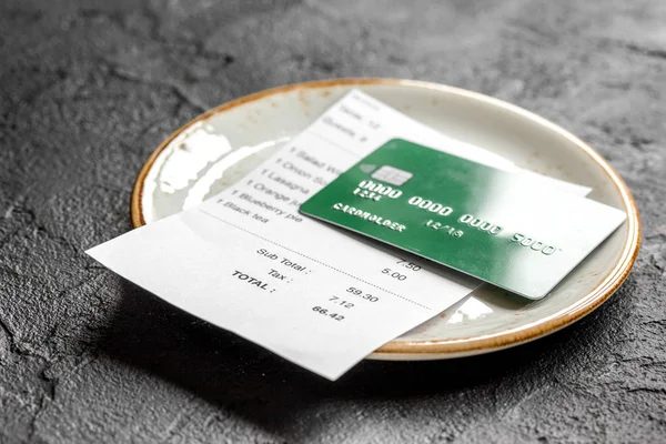 plate and receipt bill for payment by credit card dark table background