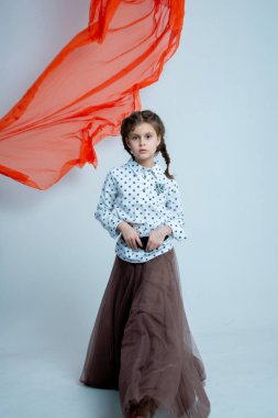 Gri arka planda fotoğraf stüdyosunda uzun etekli poz veren küçük kız model.