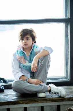 Çocuk oturuyor ve pencerenin kenarında gülümsüyor.