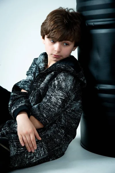 Brunet Kid Boy Sitting Black Barrel Gray Background — Stock Photo, Image