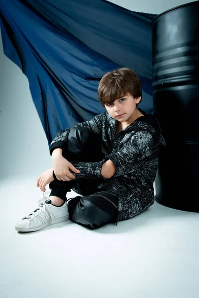 Brunet Kid Boy Sitting Black Barrel Gray Background — Stock Photo, Image