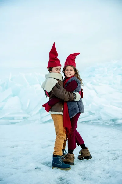Uśmiechnięte Dzieci Czerwonych Czapkach Gnoma Przytulające Się Lodzie Zimowym Tle — Zdjęcie stockowe