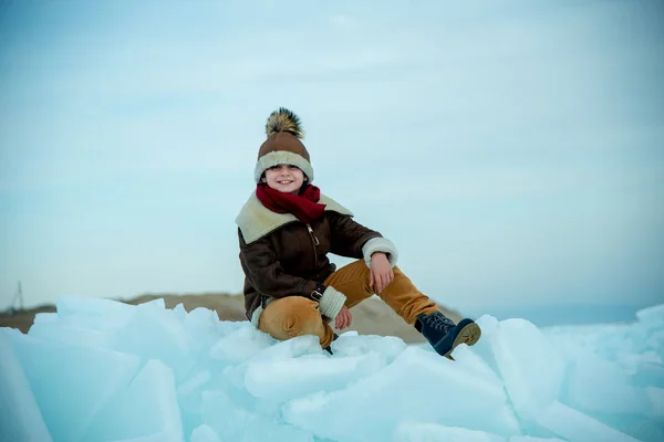 在冬天的背景下 戴着帽子坐在冰上的男孩 — 图库照片