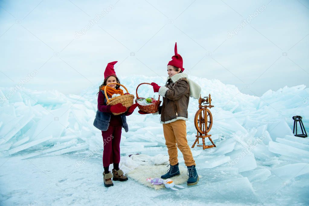 kids in red gnome caps holding picnic baskets on snow background 