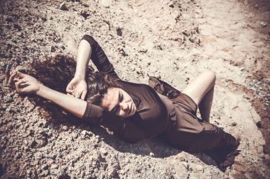 Genç kıvırcık esmer kadın taş ocağında kumlu yolda poz veriyor.