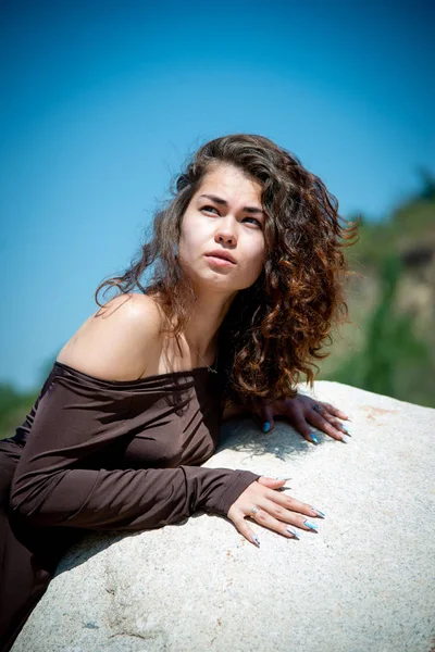 beautiful and tender woman posing on big white rock on sand background