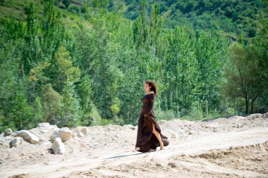 Sıska genç esmer kadın kumlu yolda yeşil ahşap arka planda