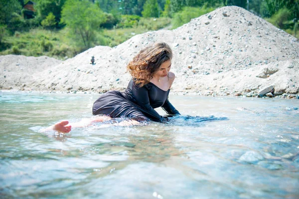 young romantic woman in wet dress lying in river on sand quarry background