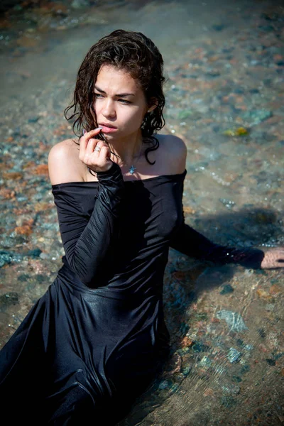 young sexy woman in wet dress posing on the river coast