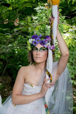 Ormanda poz veren bir çiçek çelengi içinde güzel bir gelin.