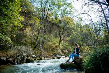 Doğada poz veren güzel bir kadın deri ceket ve kot pantolon giyiyor.