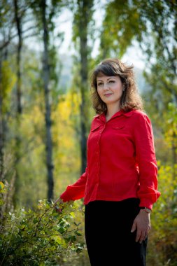 Güzel bir kadın dışarıda poz veriyor, kırmızı gömlek giyiyor.