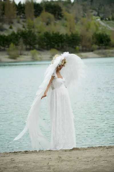 beautiful bride with angel wings posing outdoors near lake