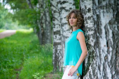 Güzel bir kadın huş ağaçlarının yanında poz veriyor.