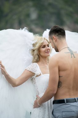 Dışarıda poz veren güzel bir çift, melek kanatlı gelin ve damat. 