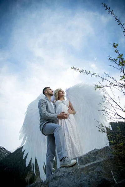 beautiful pregnant bride with angel wings posing with groom outdoors