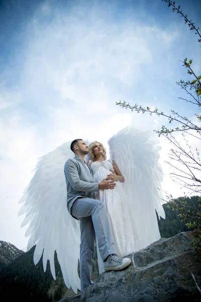 beautiful pregnant bride with angel wings posing with groom outdoors