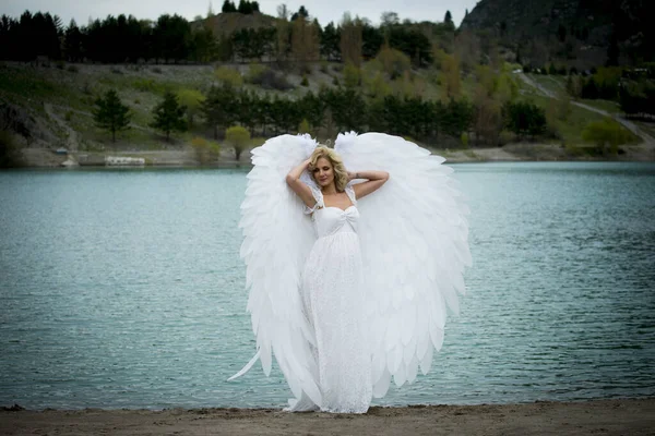 beautiful bride with angel wings posing outdoors near lake