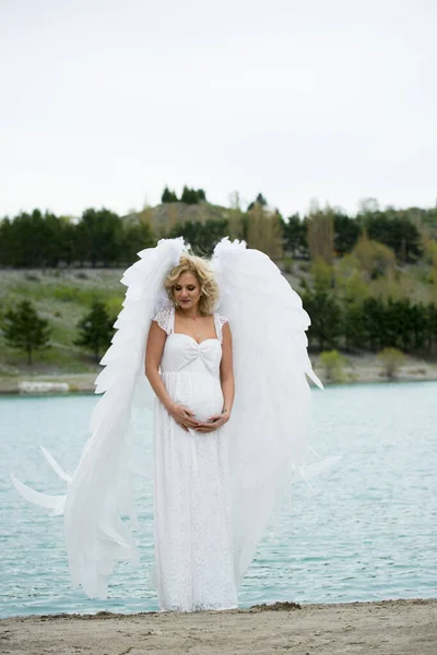 beautiful bride with angel wings posing outdoors near lake