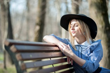 Park arka planında bankta oturan sarışın genç bir kadının portresi.