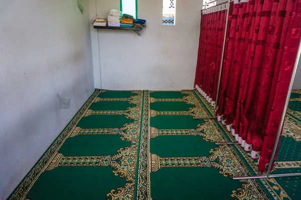 An empty mosque with green carpet and red curtain as barrier between man and woman space — Stock Photo, Image