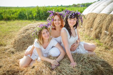 Üç genç güzel kız beyaz elbiseler ve kır çiçekleri stayingng Samanlık ve gülerek yakınındaki çelenk. Yaz Köyü