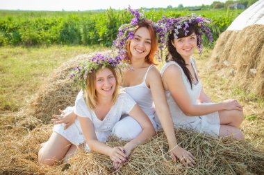 Üç genç güzel kız beyaz elbiseler ve kır çiçekleri stayingng Samanlık ve gülerek yakınındaki çelenk. Yaz Köyü