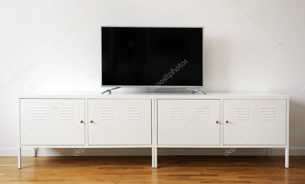 wide screen TV on white stand near light wall