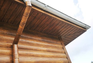 Çatı oluğu ve drenaj borusuyla metalden yapılmış. Demir kiremitlerden yapılmış bir çatı ve yağmur oluğu olan ahşap ev, yan manzarayı kapat..