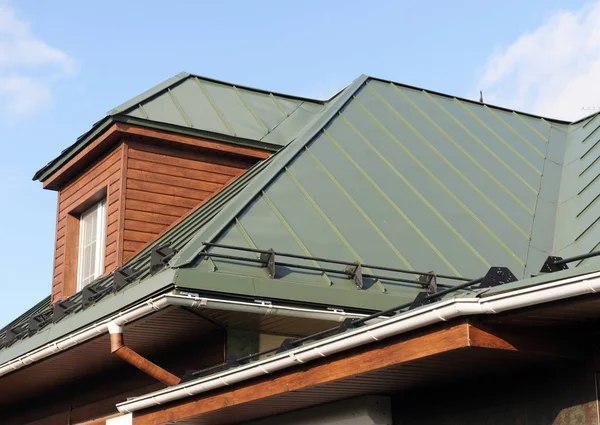 Roof made of metal with a gutter and a drainpipe. Log house with a roof made of iron tiles and a rain gutter, close up side view.