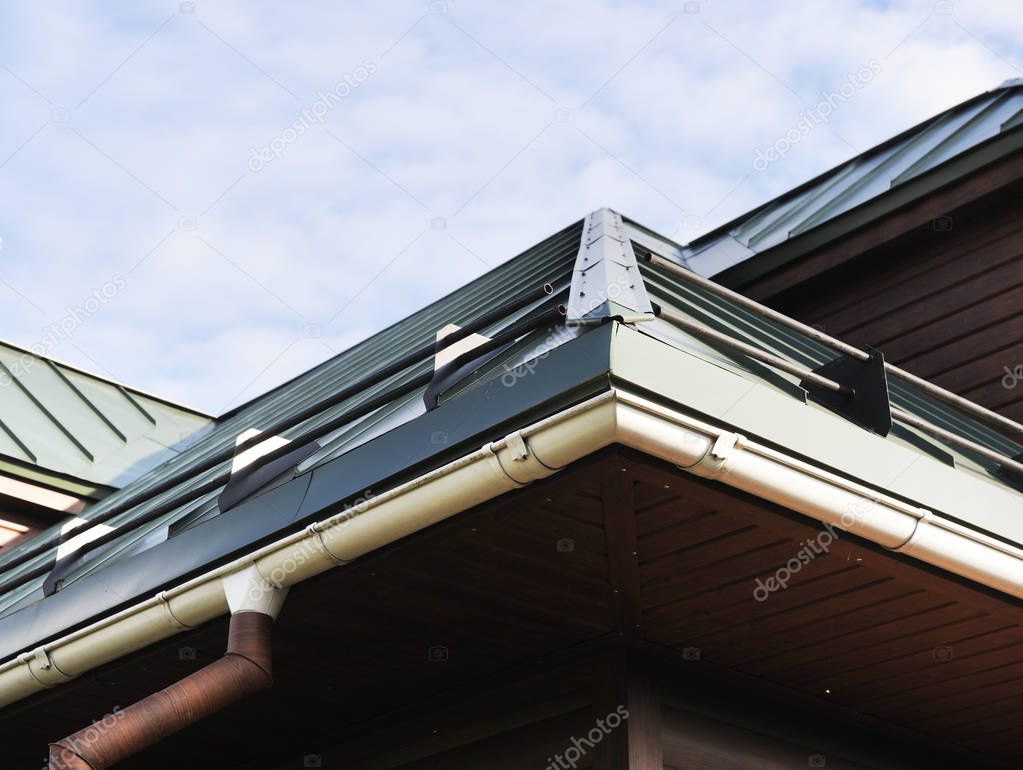 Roof made of metal with a gutter and a drainpipe. Log house with a roof made of iron tiles and a rain gutter, close up side view.