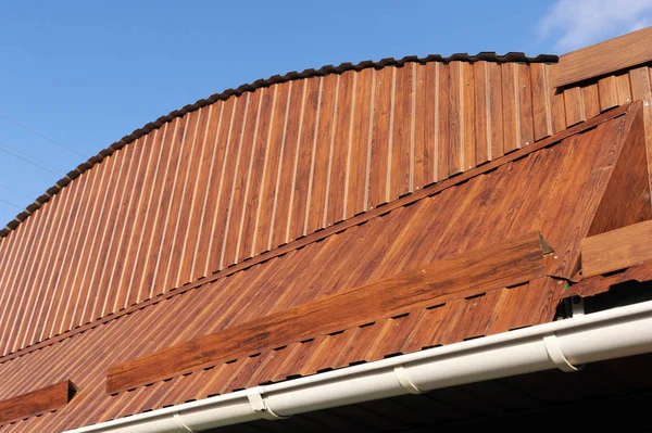 Roof made of metal with a gutter and a drainpipe. Log house with a roof made of iron tiles and a rain gutter, close up side view.