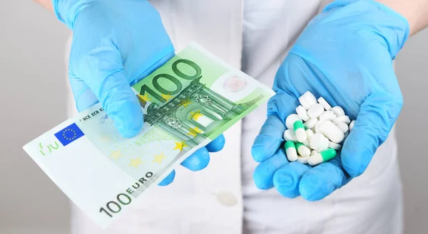 Medicine. A woman doctor in rubber gloves holds in one tablet and in another 100 one hundred euros. Life saving service, legal pharmacy, prescribes medicines. Sale of drugs in the hospital.