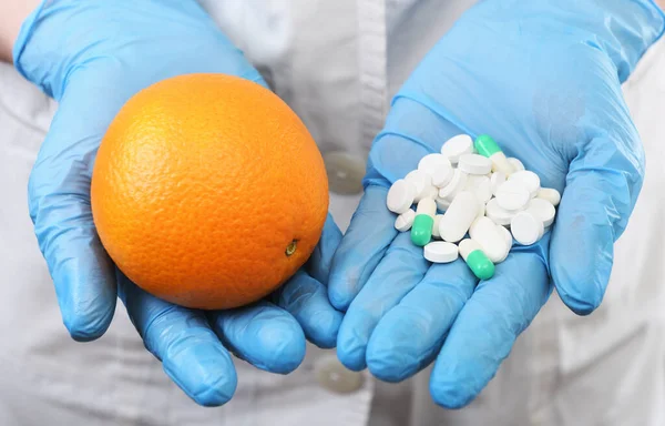 the doctor holds pills in one hand and an orange in the other